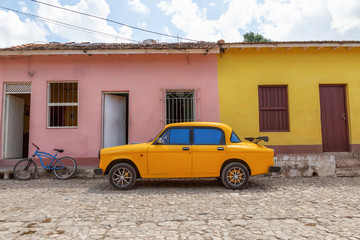 Old Yellow Car with colorful buildings in the background in a small Cuban Town during a vibrant sunny day. Taken in Trinidad, Cuba.