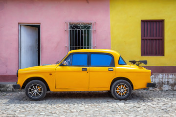 Old Yellow Car with colorful buildings in the background in a small Cuban Town during a vibrant sunny day. Taken in Trinidad, Cuba.