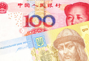 A close up image of a red, Chinese one hundred yuan note with a yellow and blue Ukrainian A Ukrainian one hryvnia bill close up in macro