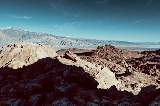 Alabama hills seen from above, with a dirty road. Mountains in the background. blue sky and desert view. 