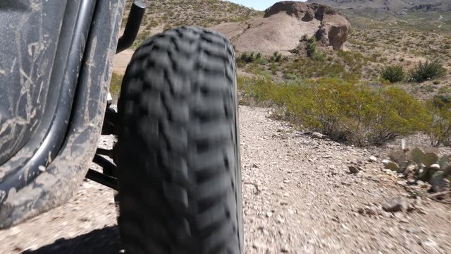ATV Lower to Ground Level with Tire. view moves down behind the front tire of an all terrain vehicle in the desert