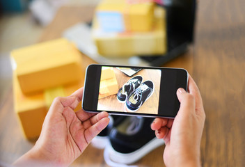 young woman taking photo sneakers with camera smartphone for post to sell online on the internet...