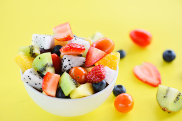 Fruit salad bowl fresh summer fruits and vegetables healthy organic food strawberries orange kiwi blueberries dragon fruit tropical grape pineapple tomato lemon on yellow