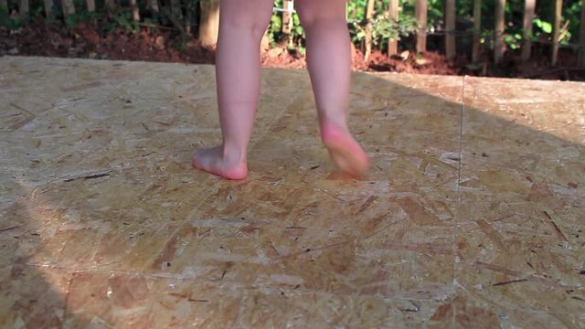 Close up of a little girl legs dancing and stomping on a wooden floor in the garden. 