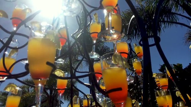 A lovely shot of a beverage tree design filled with champagne flutes which contain mango fruit puree, champagne and a dash of grenadine, garnished with a lemon. A nice parallax through sun glare.
