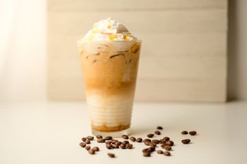 Ice coffee in the glass topped whipping cream with coffee beans. Cold summer drink on wooden background and copy space. Advertising for caramel mocha and chocolate beverage for the cafe.