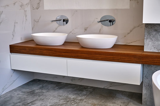 Luxury Bathroom Vanity. Ceramic Round Sinks Placed On Teak Tabletop In Luxury Bathroom With Gray And White Marble Walls