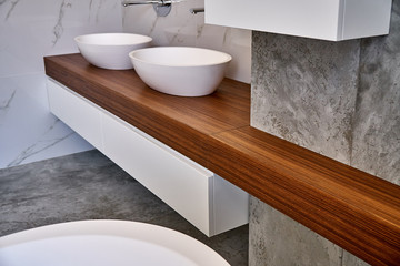 Luxury bathroom vanity. Ceramic round sinks placed on teak tabletop in luxury bathroom with gray...