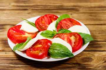 Italian caprese salad with tomatoes, mozzarella cheese and basil on a wooden table