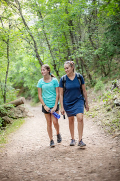 Mother and daughter hiking together along a scenic mountain trail on a summer day. Lifestyle photo of people outdoors enjoying nature and being active