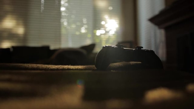 Video game controller on couch with sun coming through trees and blinds into family living room.