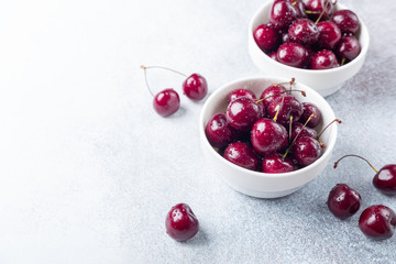 Fresh ripe red cherries in a white bowl on a gray stone background Closeup Water drops
