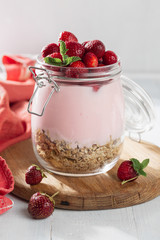 Granola yogurt with homemade strawberry in glass jar on a wooden board in home kitchen