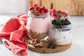 Granola yogurt with homemade strawberry and blueberry in glass jar on wooden board in home kitchen