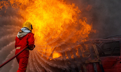 Brave firefighter using extinguisher and water from hose for fire fighting, Firefighter spraying high pressure water to fire, Firefighter training with dangerous flames, Copy space-Image - obrazy, fototapety, plakaty