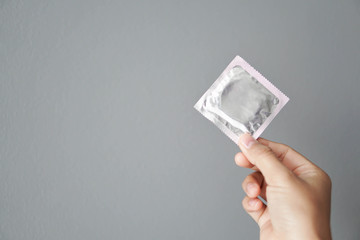 Close up hand holding condom with grey background, health care and medical concept