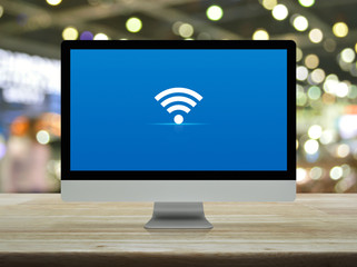 Wi-fi flat icon on desktop modern computer monitor screen on wooden table over blur light and...