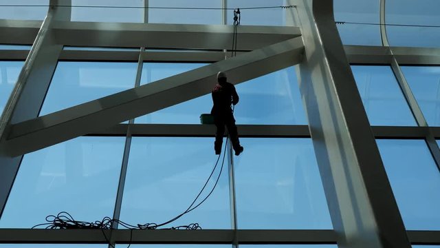 faceless worker man is washing windows with scraper on a highrise modern building hanging the rope.