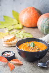 Pumpkin soup in a black plate on a stone background. Autumn decorations.