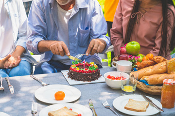 Grandfather with birthday cake celebrating in family party at home garden