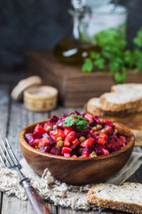 Russian beetroot salad vinaigrette in wooden bowl with rye bread, rustic background