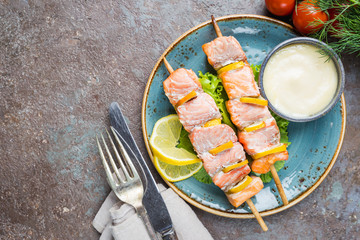 Grilled skewers of salmon with lemon and sauce on dark stone background, top view with copy space