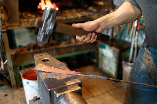 Blacksmith forging red-hot metal with hammer.