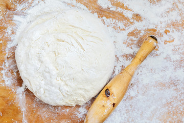 Rolling pin, dough and flour on wooden board.