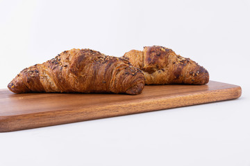 Two freshly baked croissants with sesame seeds on an insulated cutting board