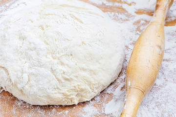 Rolling pin, dough and flour on a wooden board close-up.