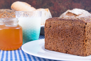 Colorful photo of a piece of multigrain bread accompanied by yoghurt and a jar of jam.