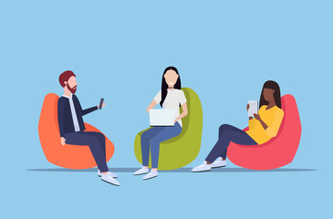Obraz na płótnie Canvas businesspeople sitting in bean bag armchair mix race colleagues team using digital gadgets social media communication concept flat full length horizontal