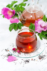 fragrant tea with wild rose in a glass cup on a white background, vertical top view