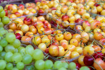 Ripe white yellow sweet cherries and grapes for sale at farmers market