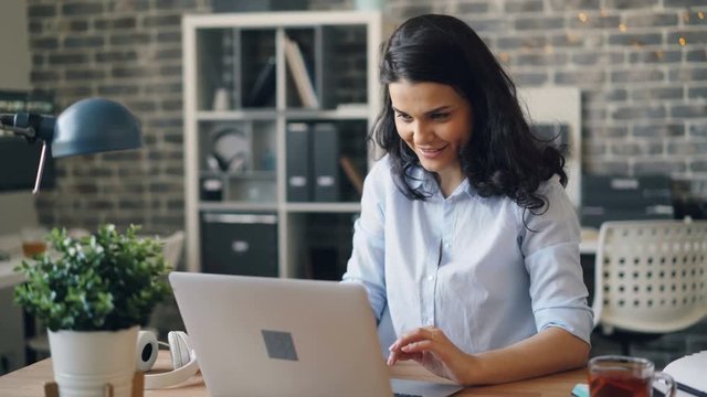 Happy girl is getting good news on laptop clapping hands laughing having fun celebrating success sitting at desk in office. People, achievement and youth concept.