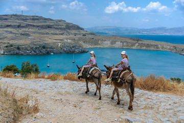 Two twin girls riding donkeys on a mountain road to the sea. Lindos. the island of Rhodes. Greece....