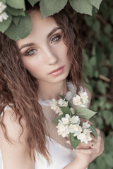 Obraz na płótnie Canvas beautiful cute tender girl with dark hair in a white summer dress with a jasmine flower in hands