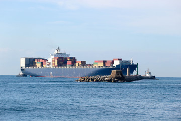 Large cargo container ship with two tugboats entering the Livorno port, Italy