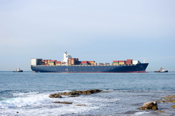 Large cargo container ship with two tugboats entering the Livorno port, Italy