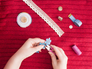 Woman cuts off blue lace on background of red wool fabric dress