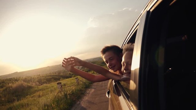 Happy family traveling by car. Two boys in the car window waving their hands in the sun at sunset.