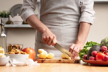 The chef prepares a vegetarian salad with the hand of a chef in the home kitchen. Light background with text area for restaurant menu design. The concept of healthy eating, cooking salad