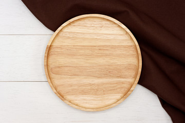 Empty round wooden plate with dark brown tablecloth on white wooden table. Top view image.