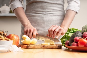 The chef cooks, cuts an apple, in the process of a vegetarian salad with the hand of the chef in the home kitchen. Light background for restaurant menu design, menu, recipe book