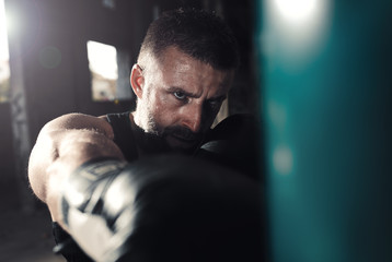 Male boxer punching a boxing bag in warehouse.