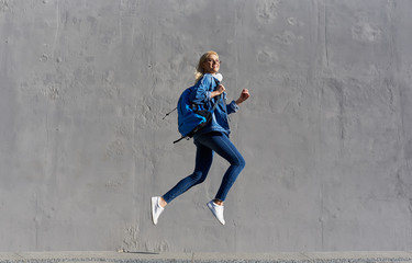 Full body Portrait of happy young woman walking with bag and cellphone. Cheerful student  jumping in air over gray background
