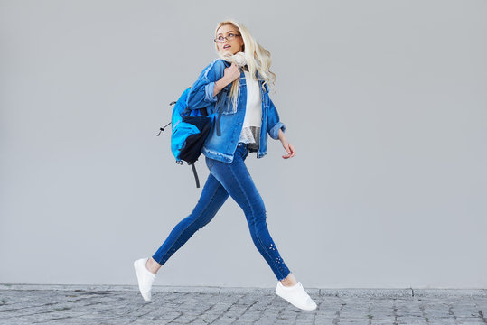 Full body Portrait of happy young woman walking with bag and cellphone. Cheerful student  running in air over gray background
