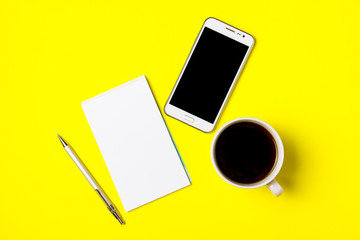 Smartphone, notepad and cup of coffee on a yellow background. Top view