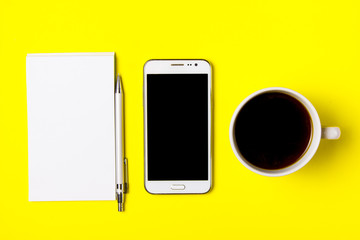 Smartphone, notepad and cup of coffee on a yellow background. Top view