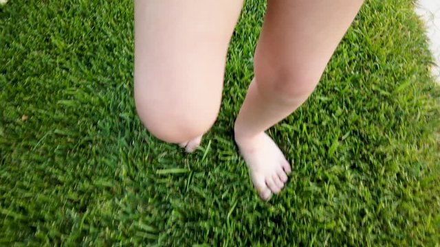 Feet of little girl while walking on grass in park or garden